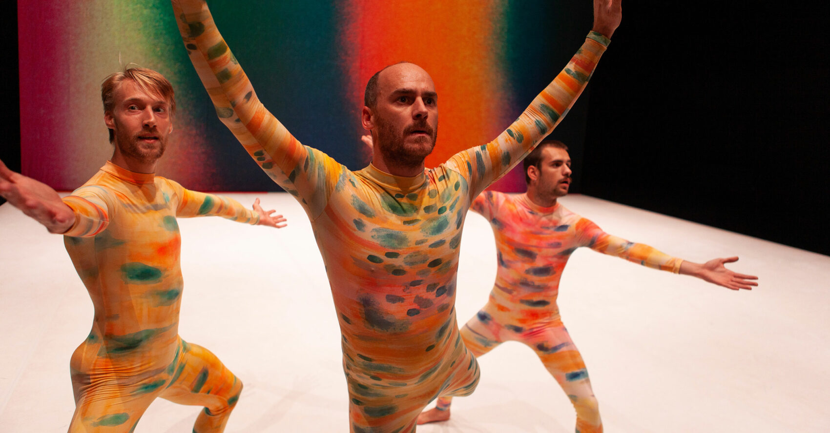 Les trois danseurs en pose avec les bras en l'aire avec des académiques jaune avec des taches oranges et vertes